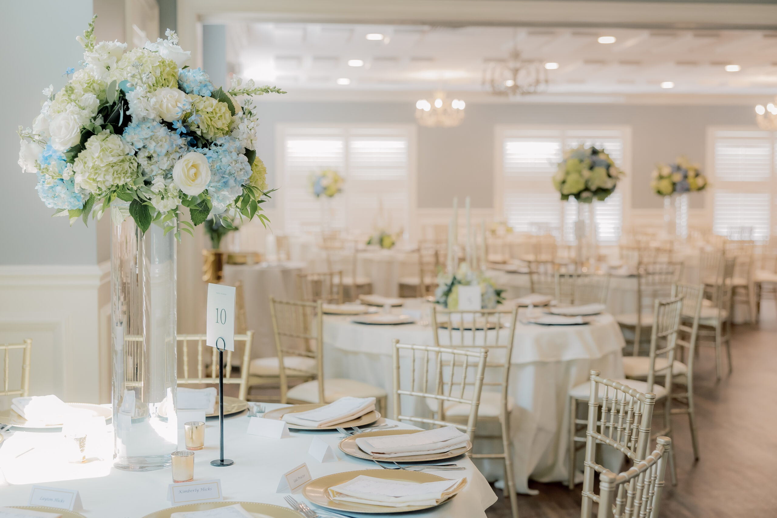 Wedding reception tables with large white and blue floral centerpieces.